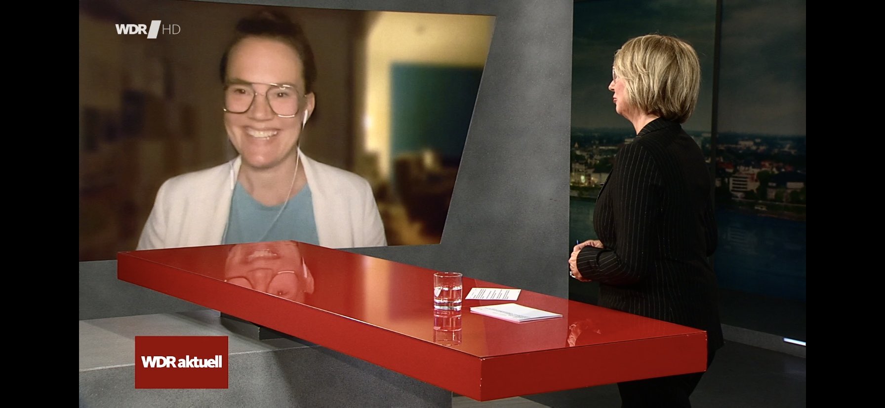 Screenshot der Interviewsituation. Ich schaue zugeschaltet in die Kamera, die Moderatorin dreht sich mi rzu und den Rücken zum Publikum.