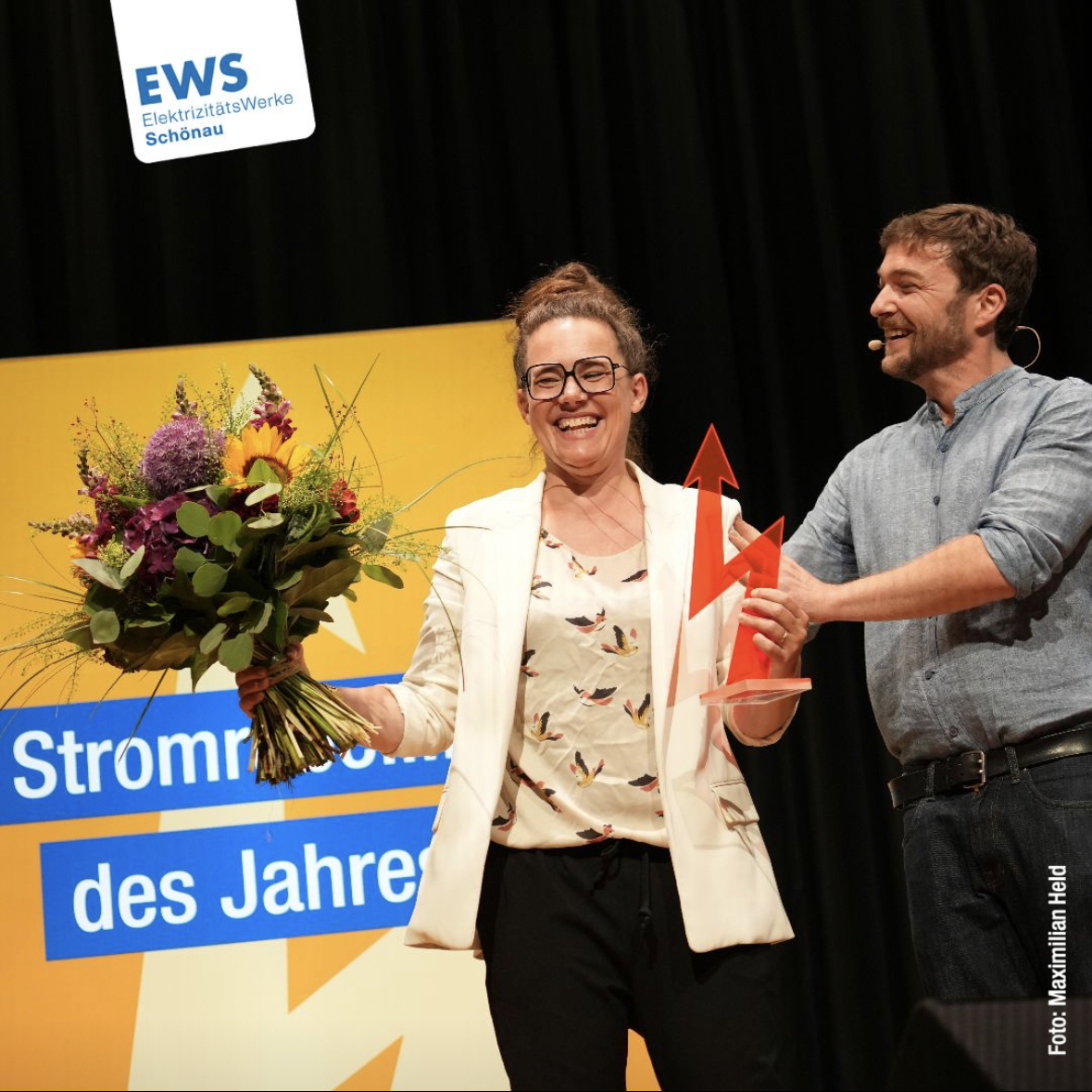 Foto der Preisübergabe, ich halte den roten Blitz, den Preis, und einen Blumenstrauß, den Sebastian Sladek mir übergibt. Foto: Albert Josef Schmidt
